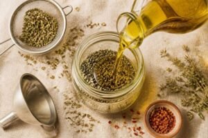 Huile d'olive versée sur de l'origan séché dans un bocal en verre, avec une passoire, un entonnoir et un bol de piment séché
